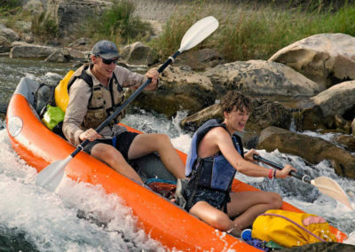 couple in lifejackets rowing down rapids in canoe