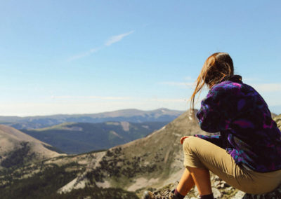 girl sits on rock overlooking mountain valley