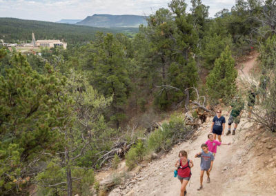 family hikes along trail with view of Glorieta Mesa and main camp in background