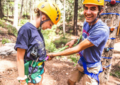 summer staff counselor tightening knot on camper's safety harness