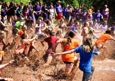 large group of kids representing different team colors rush into the middle of the mud pit