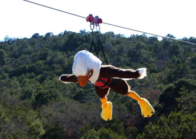 glorieta mascot baldy the eagle in full body harness riding the zip tour over trees