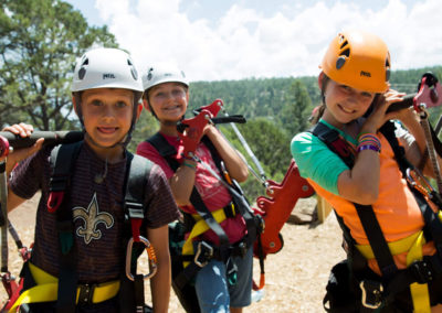 young students in harnesses and helmets carry zip tour gear