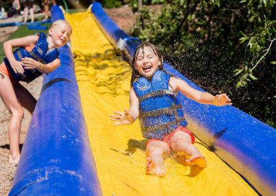 day camp camper girl closes her eyes and smiles splashing through water on water slide