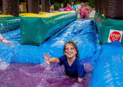 young camper slides into purple water off inflatable