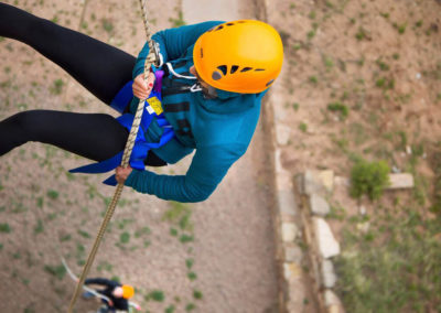 girl in helmet and harness rappelling down wall