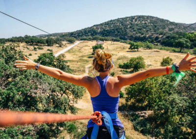 girl in harness spreads arms in preparation to go on zip line