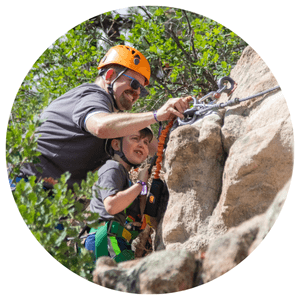 father and son in harnesses on the side of a rock