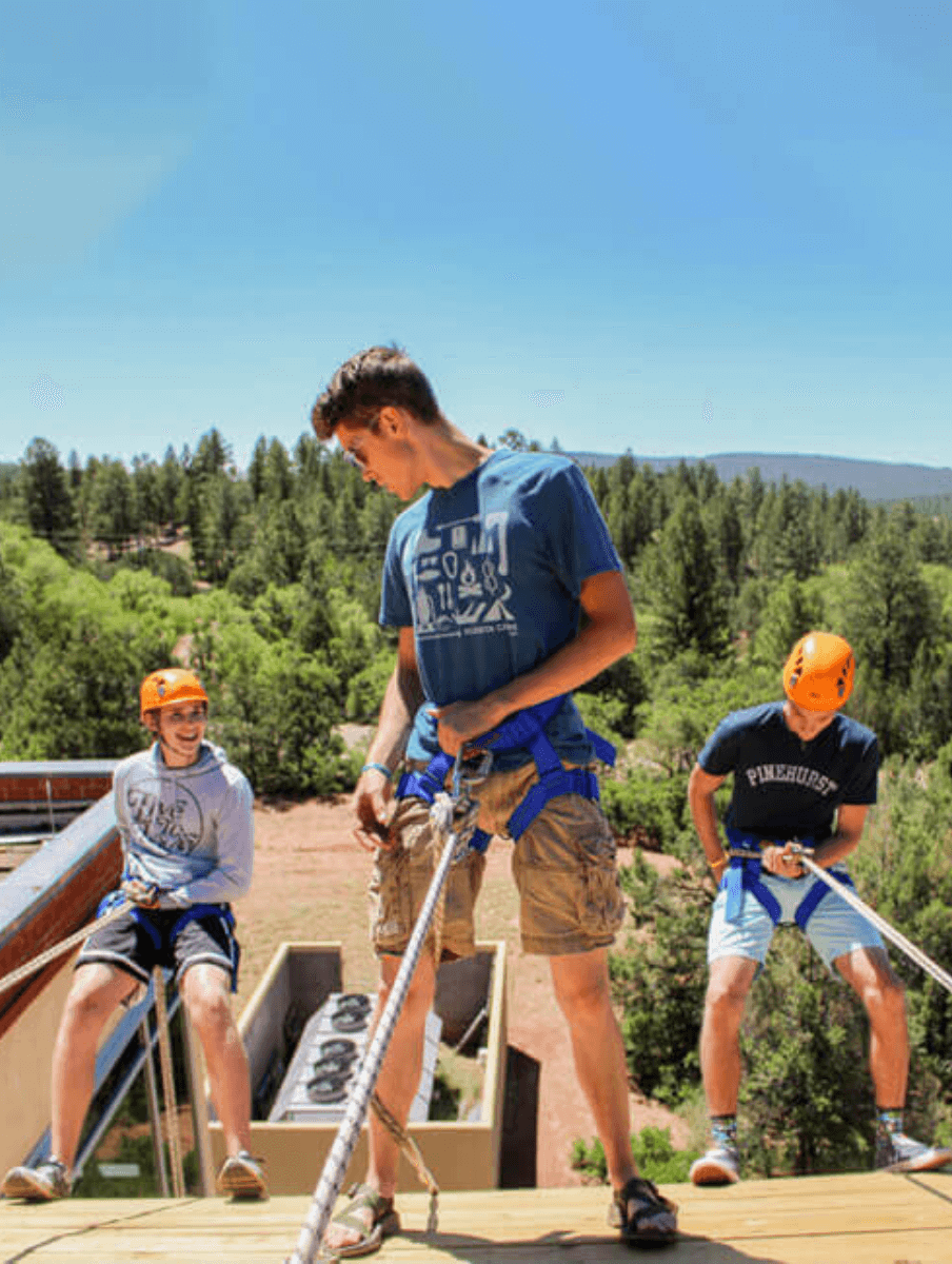 people repelling off a building with trees in the background